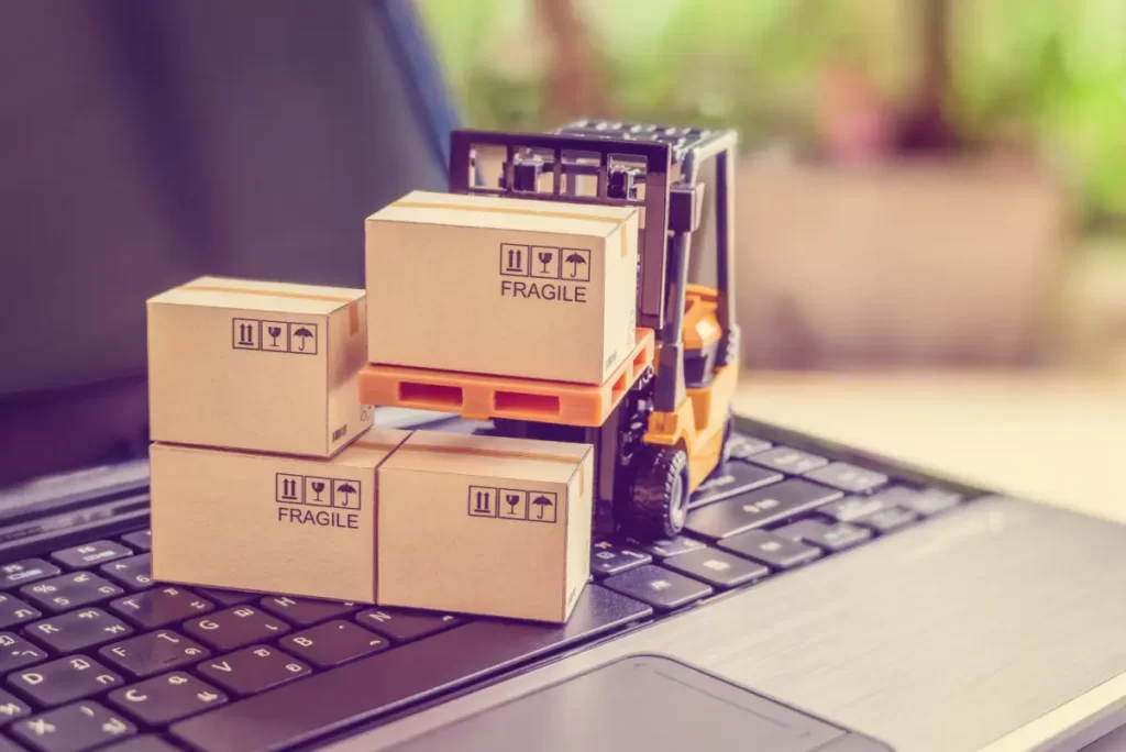 black laptop with boxes stacked and yellow toy forklift lifting yellow plastic pallet with box on it